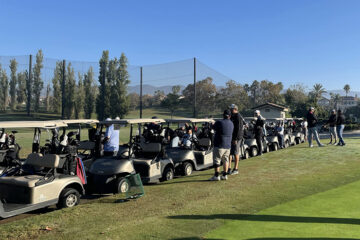 Image of golf carts and men standing near carts on golf course.