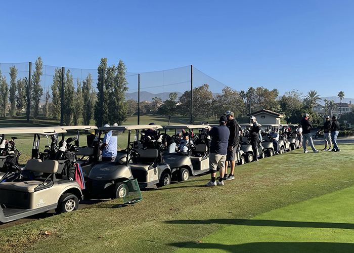 Image of golf carts and men standing near carts on golf course.